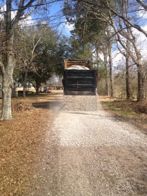 Dump truck tailgate-spreading gravel down a wooded lane